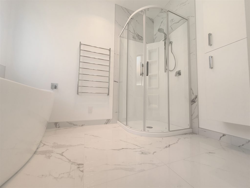 Curved acrylic shower with exterior tiling to the ceiling. Note the shower has a corner moulded shelf built into the wall liner.