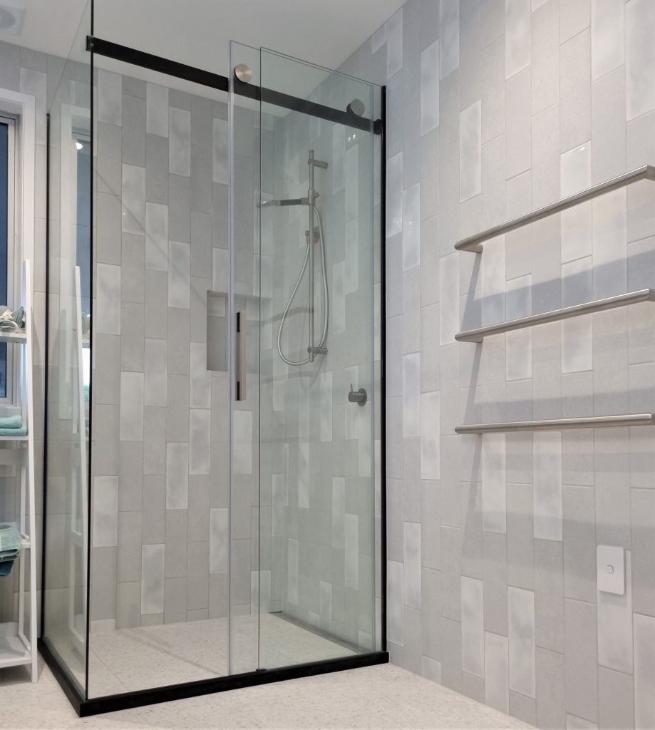 This is a fully tiled (floor and wall) Atlantis shower with a channel drain. We have put a tiled niche into the wall here, (niche = recessed shelf into the wall). Featuring a sliding shower door for access. The hardware on this shower is coloured (black).