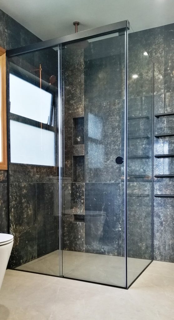 This shower has a full tiled wall and level entry floor, two niches plus a foot rest niche, coloured hardware and sliding door. 