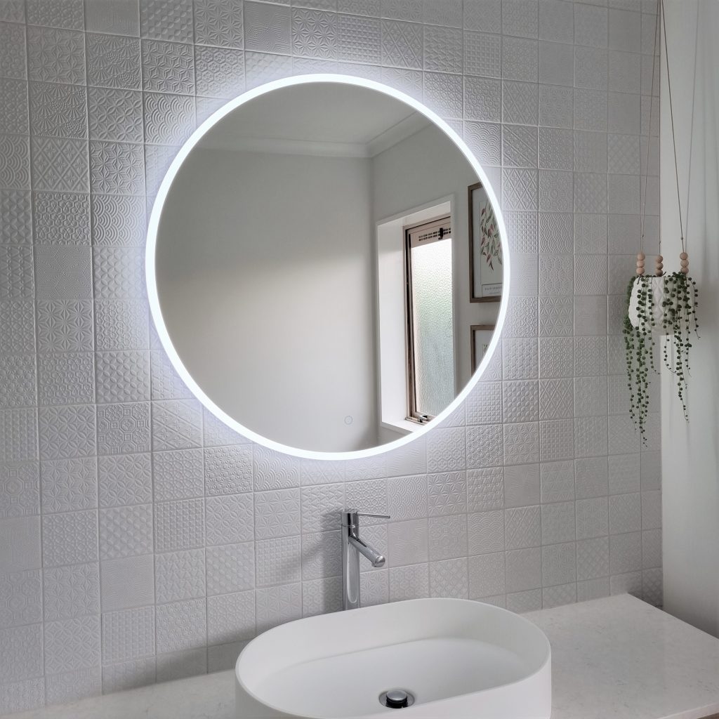A LED mirror installed over a tiled wall, slab vanity and vessel basin